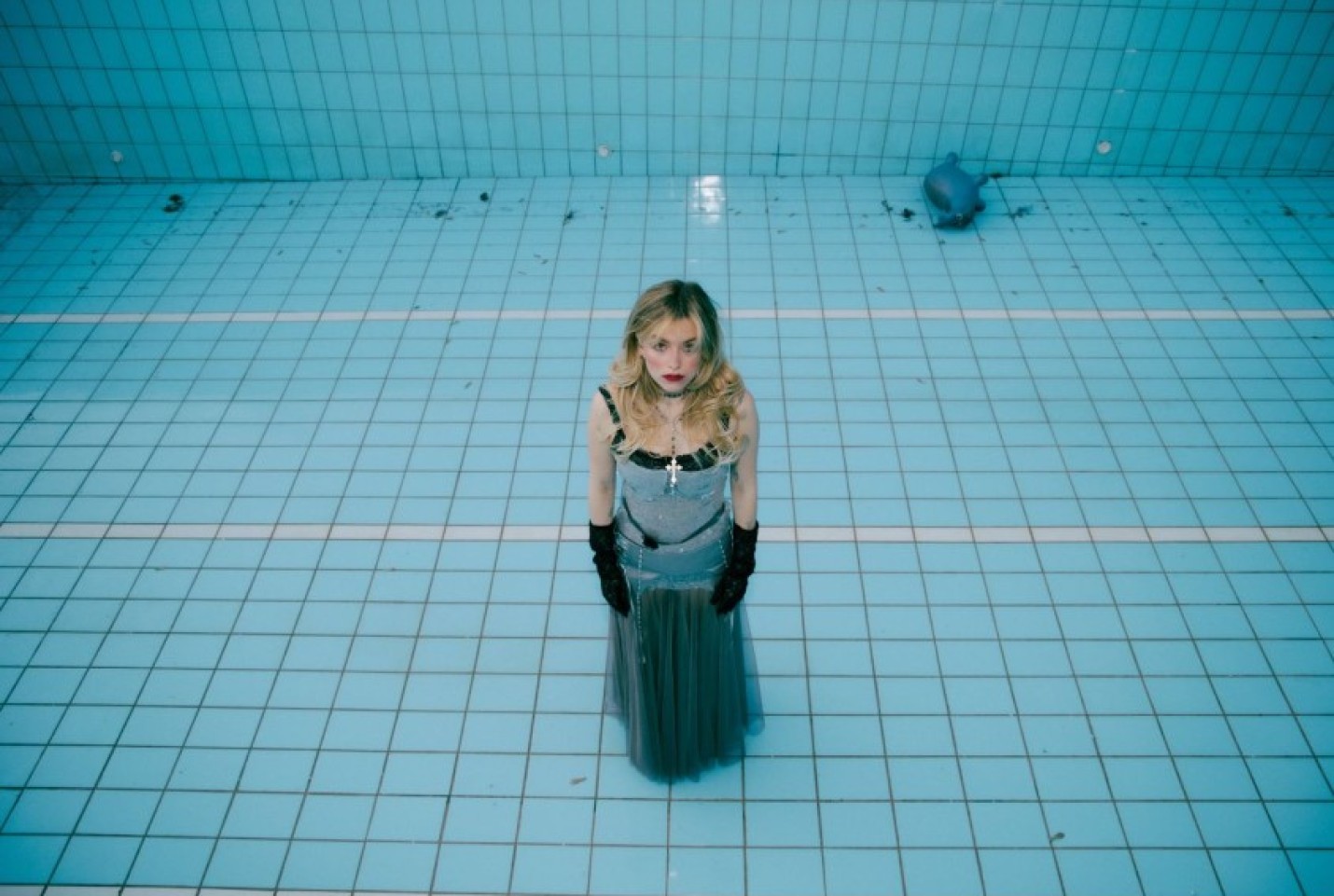 Elieen Alister standing at the bottom of a swimming pool in a dress and black gloves.